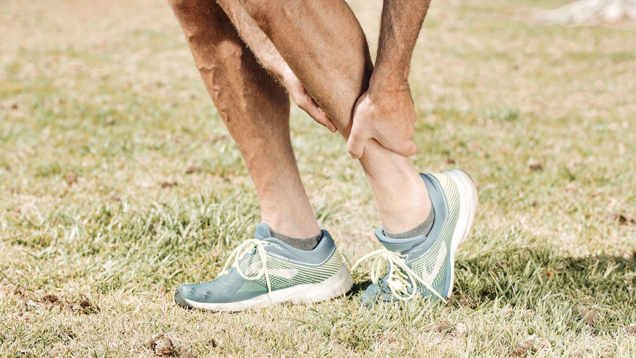 Läufer in Sportschuhen greift sich auf einer Wiese an die schmerzende Wade als Symbolbild für CBD zur Muskelentspannung