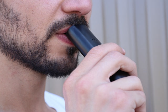 Nahaufnahme eines bärtigen Mannes, der an einem schwarzen Vape Pen zieht, als Symbolbild zum Test von Einweg CBD Vapes