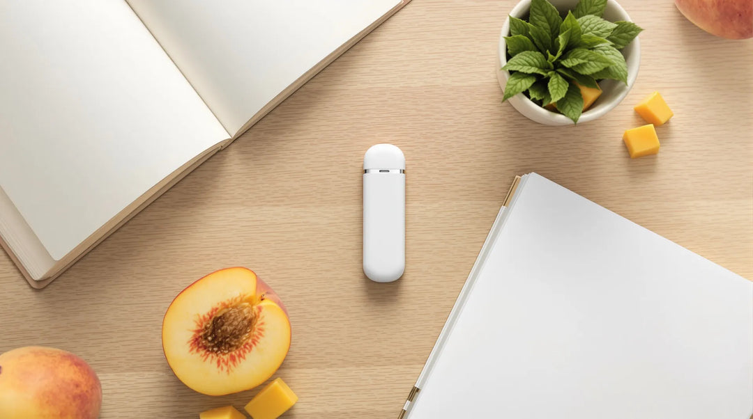 Weißer Vape-Pen ohne Aufdruck zwischen aufgeschlagenem Notizbuch, halbiertem Pfirsich, Mangowürfeln und Minze auf hellem Holz, Titelbild zu OBEE Vape Erfahrungen